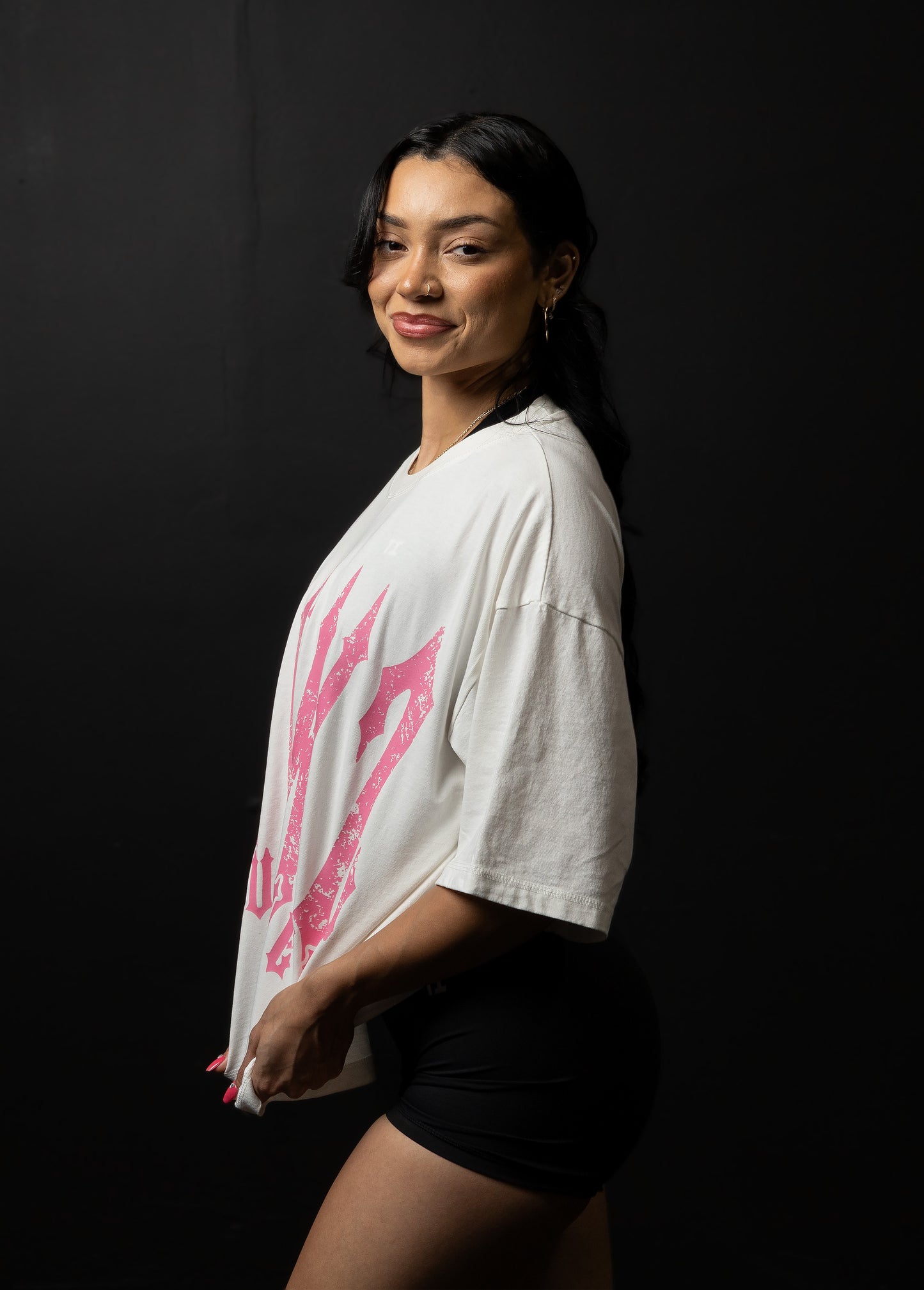 Woman wearing a white shirt with pink graphics and black shorts against a dark background