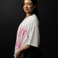 Woman wearing a white shirt with pink graphics and black shorts against a dark background